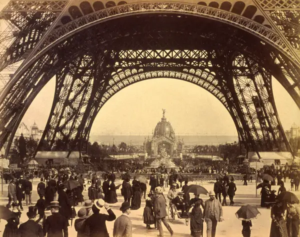 Crowd of people walking under the base of Eiffel Tower, view toward the Central Dome, Paris Exposition